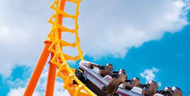 Das Bild zeigt eine Achterbahn mit einem Wolkenhintergrund
